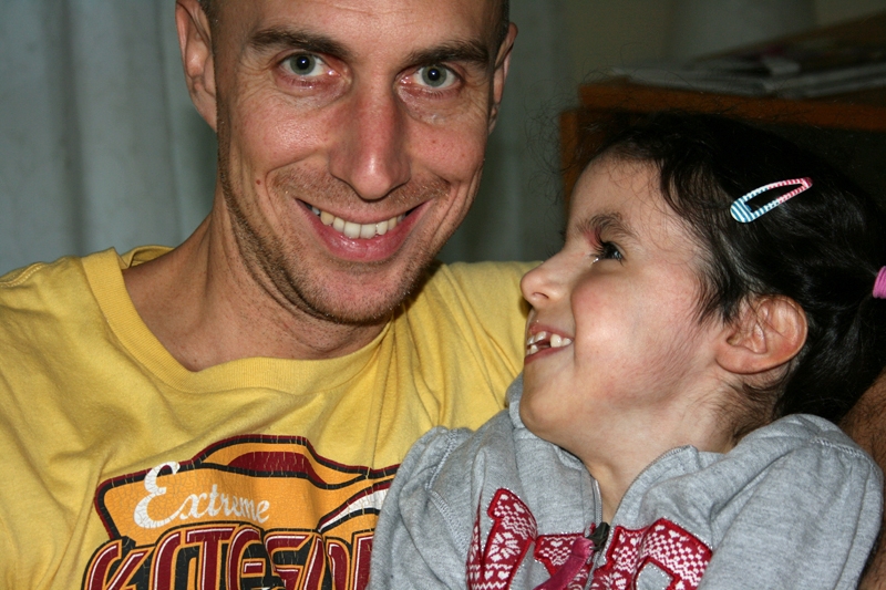 Wolfgang lächelt in die Kamera, seine Tochter Jaël (Trisomie) ist auf seinem Arm und lächelt ihn von der Seite an.
