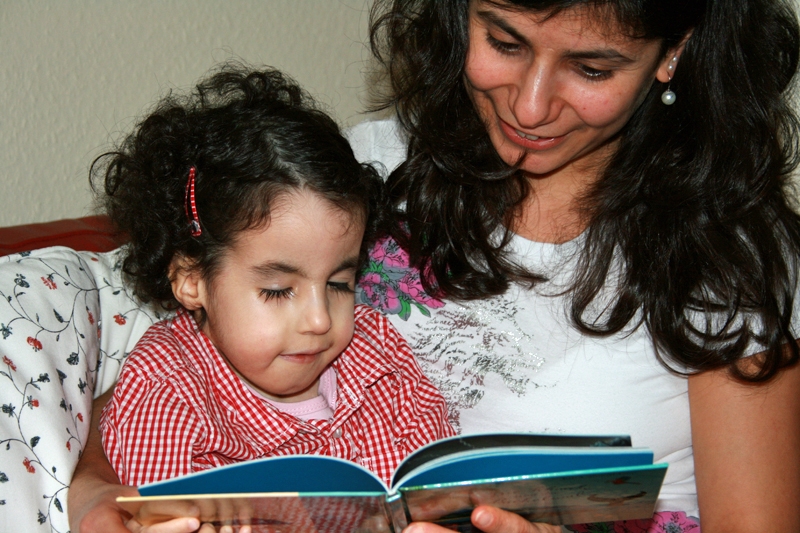 Jaël (Trisomie 18) mit 7 Jahren, auf dem Arm ihrer Mama, schaut sich ein Buch an, das ihre Mama hält.